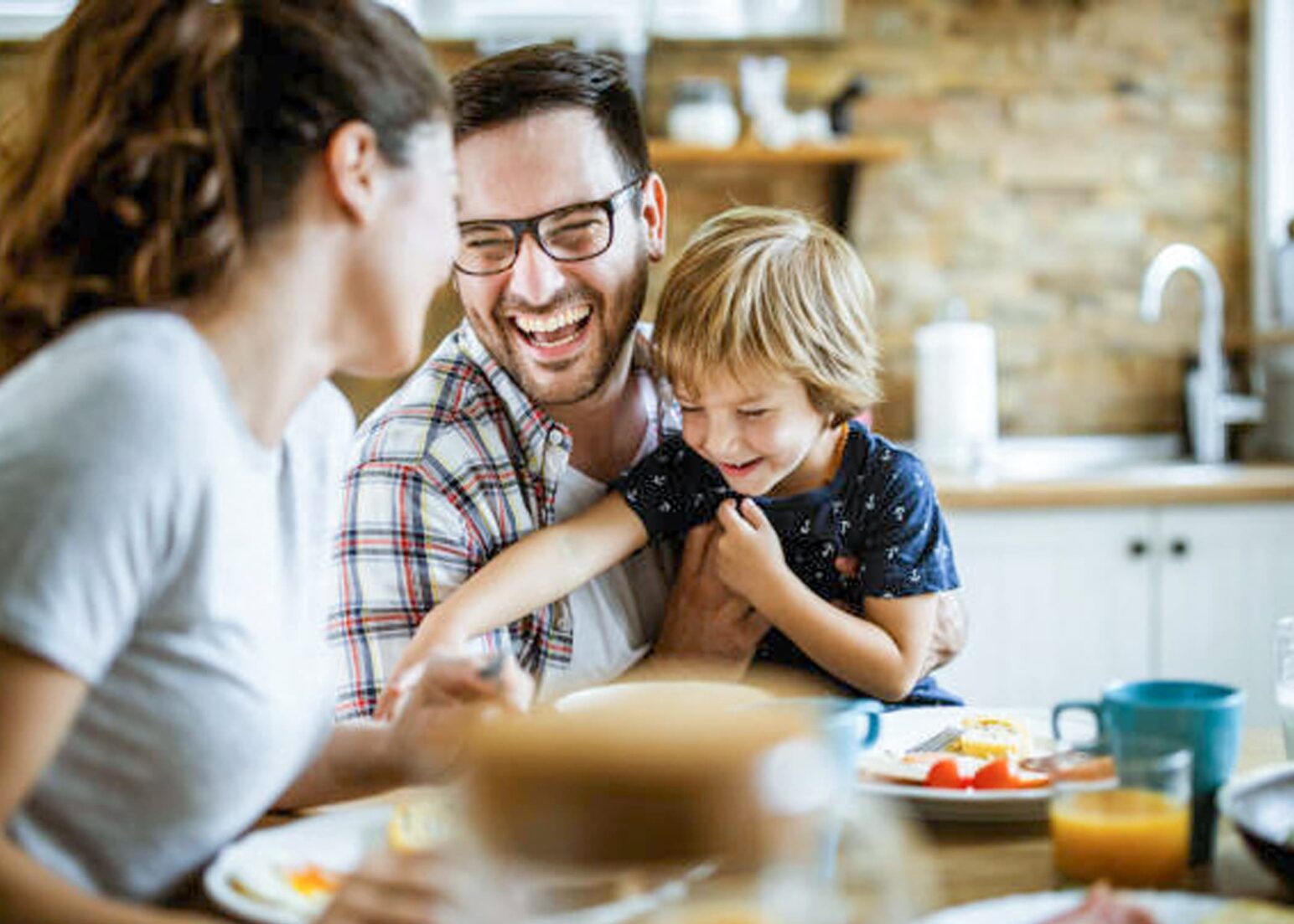 Famille riant à table, homme tenant son fils tout en regardant sa femme